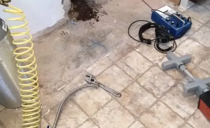 Leak detection equipment next to a cut-open section of tile where a slab leak was traced