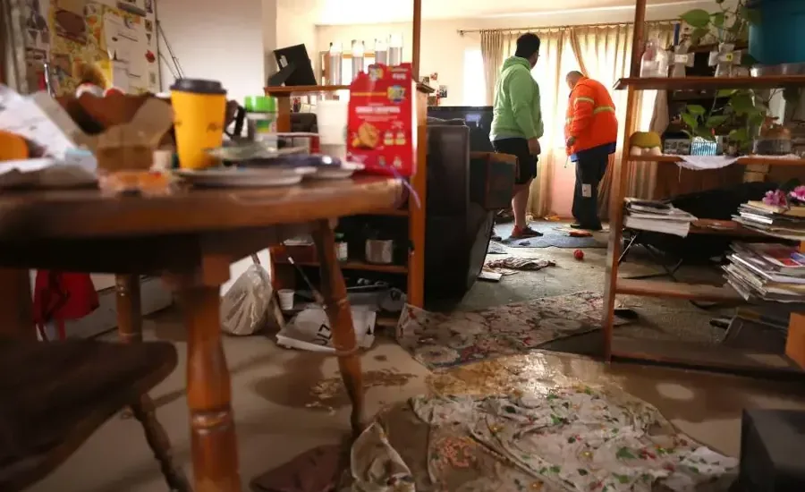 Workers clearing a wet, littered living room after storm floodwater came in